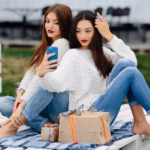 two-women-sit-bench-outside-shoot-gifts-smartphone_1153-5601